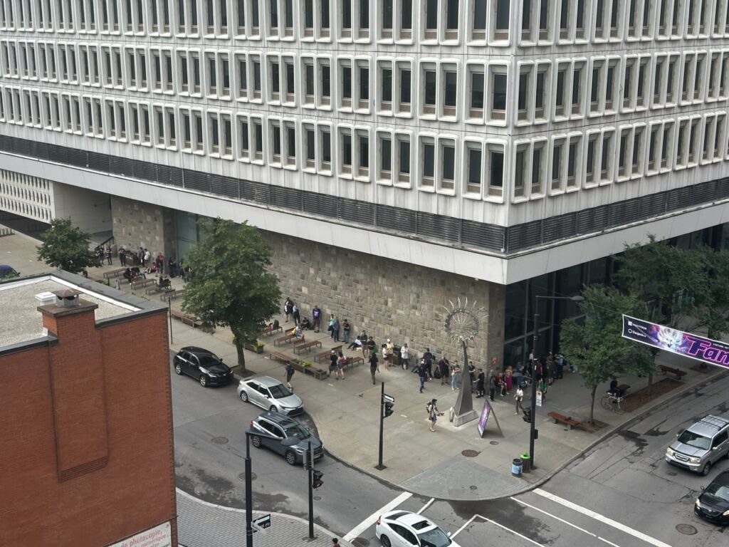 View of a modernist college building with a line of people curved around the corner.