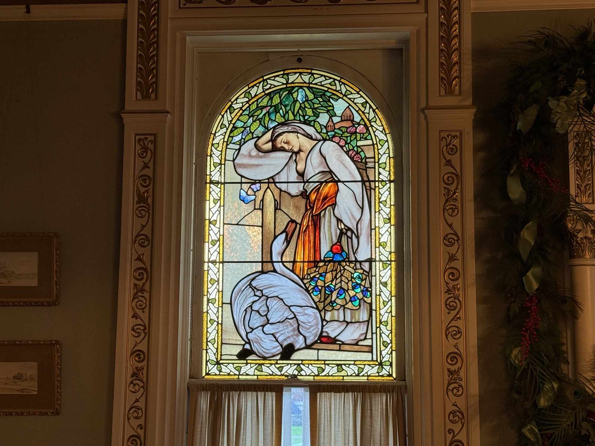 A stained glass window depicting a woman with a swan; she’s holding a bunch of peacock feathers. It’s based on a pre-Raphaelite painting called The Odalisque by Sir Frederic Leighton.